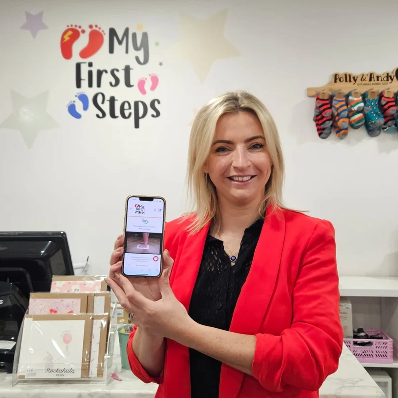 Woman holding a phone displaying SizeWise in the My First Steps shoe store